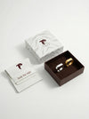 Jewelry set with two rings in a box, accompanied by branded card and box on a light gray background.