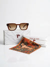 Sunglasses with a branded box and tiger-themed scarf on a white background