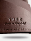 Close-up of a brown leather product with 'TUcc made in Bangladesh' embossed on it.