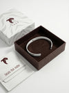 Silver bracelet in a brown box with Tucc branding on a white background